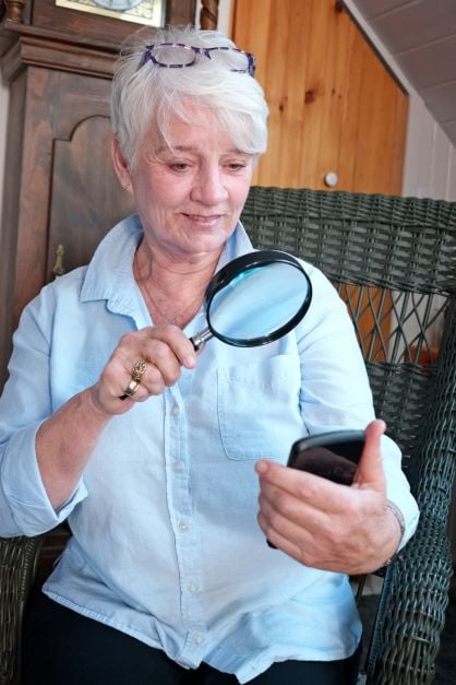 รูปหญิงชราใข้แว่นขยายดูโทรศัพท์มือถือ หนึ่งในกลุ่มคนที่มี Accessible Barrier